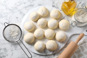 Raw dough balls, flour, rolling pin and oil on white marble table, top view