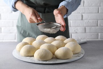 Woman sprinkling flour over dough balls at grey table, closeup