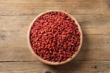 Dried goji berries in bowl on wooden table, top view
