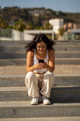 Chica joven en verano sonriendo haciendo fotos con el móvil en un lugar de mar y bonito. Pelo rizado y brillante. 