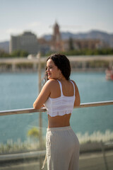 Chica joven en verano sonriendo haciendo fotos con el móvil en un lugar de mar y bonito. Pelo rizado y brillante. 