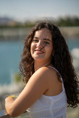 Chica joven en verano sonriendo haciendo fotos con el móvil en un lugar de mar y bonito. Pelo rizado y brillante. 
