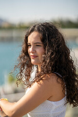 Chica joven en verano sonriendo haciendo fotos con el móvil en un lugar de mar y bonito. Pelo rizado y brillante. 