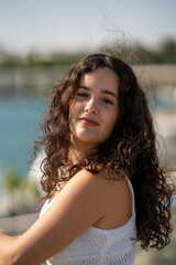 Chica joven en verano sonriendo haciendo fotos con el móvil en un lugar de mar y bonito. Pelo rizado y brillante. 