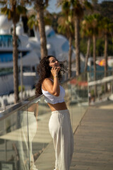 Chica joven en verano sonriendo haciendo fotos con el móvil en un lugar de mar y bonito. Pelo rizado y brillante. 