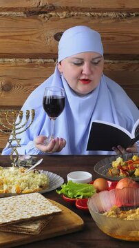 A Jewish woman in a blue veil at the Pesach Seder table reads kiddush with a glass of win