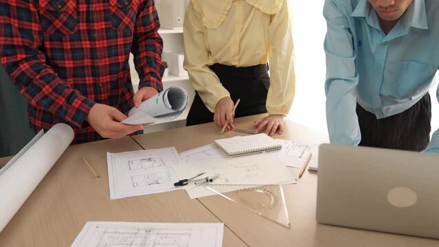 Professional engineer team discussion about house design on meeting table with architectural equipment and building blueprint scatter around at modern office. Focus on hand. Closeup. Delineation.
