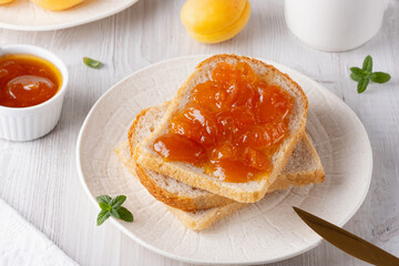 Apricot jam on bread in a white plate and a jar of apricot jam