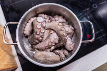 From above of whole raw octopus boiling in pot on modern black induction cooker