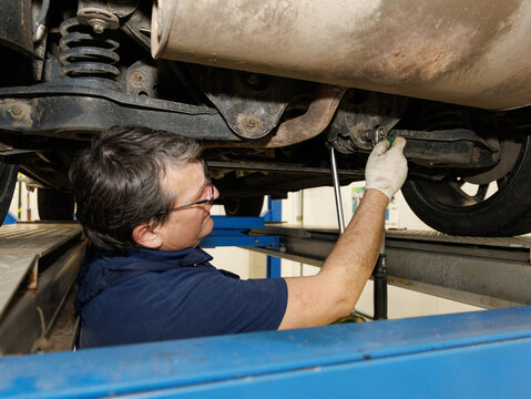 An adult professional mechanic at a car service repairs wheel alignment and adjusts camber bolts
