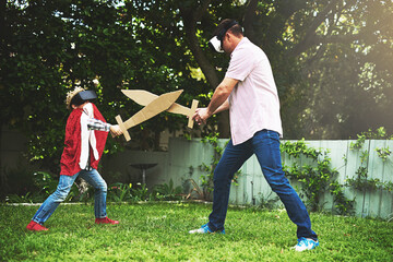 Father, son and play fighting with sword for bonding or VR in costume, cosplay or backyard at home. Fun dad, child or little boy enjoying outdoor game on grass field, lawn or virtual reality at house
