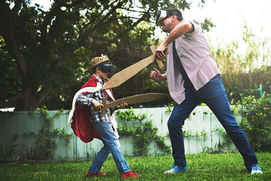 Father, son and playing with sword for fight, VR or bonding in costume cosplay or backyard at home. Fun dad, child or little boy enjoying outdoor game on grass field, lawn or virtual reality at house