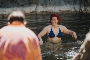 Woman with red hair in a blue bikini smiling while swimming in a natural water body, accompanied by a friend wearing an orange shirt.