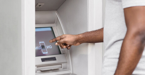 A man uses an ATM machine, pointing his finger at the screen.