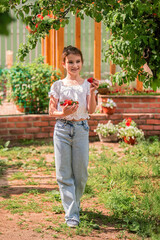 girl holds a bowl of strawberries and smiles in the garden.