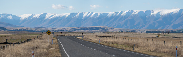 Open road through Otago high country with snow capped Southern Alps, New Zealand