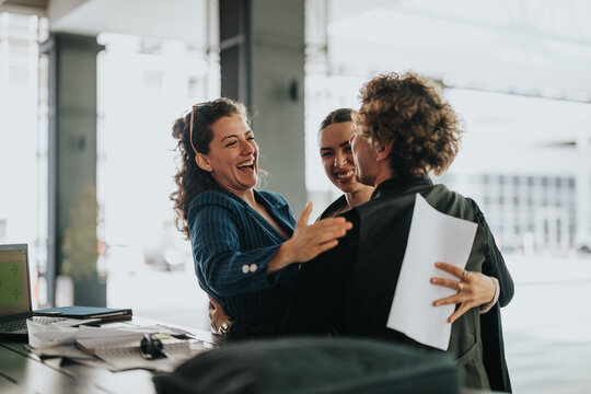 Group of cheerful business professionals sharing a joyful hug, celebrating success and teamwork in a modern office setting.
