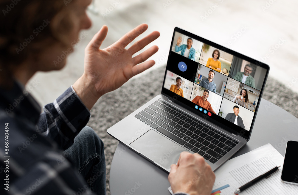 Poster a man sits at a desk in front of a laptop, actively participating in a video conference meeting. lap