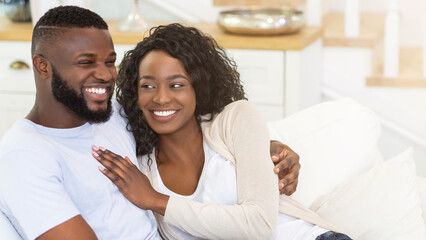 Fototapeta premium A happy couple sits on a white couch in their home, looking relaxed and enjoying each others company.