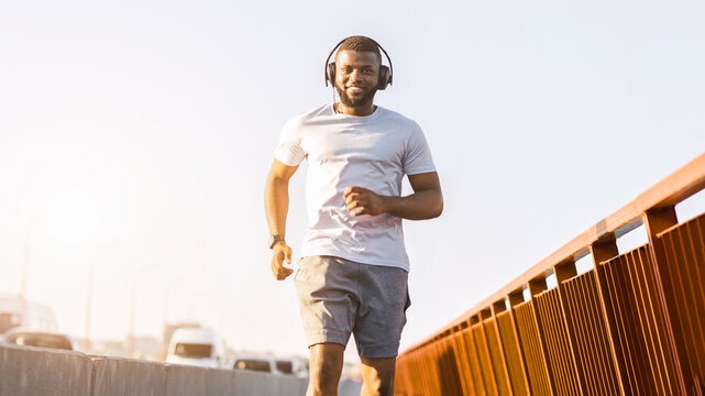Cheerful african american young man enjoying jogging by the city, running by bridge, copy space