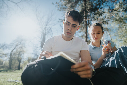 Focused high school students engaged in collaborative study outdoors on a sunny day, working on a school project together.