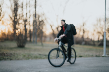 Fototapeta premium A blurred image captures a man biking through a serene park during sunset, highlighting a moment of tranquility and escape from daily life.