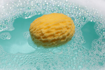 Yellow bath sponge floating on blue water with soap foam