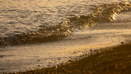 sea waves breaking on the sandy beach with sepia coloured water at sunset	