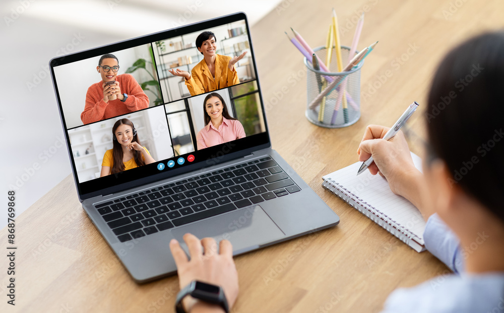 Poster woman takes notes on a notepad while participating in a video conference meeting on a laptop compute
