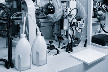 Two white bottles of glue are on the table next to the machine. The machine is surrounded by wires...