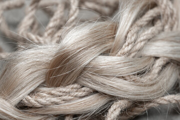 Blonde hair intertwined with jute rope, creating a unique texture contrast. This visually intriguing image is suitable for themes of natural materials, beauty, and artisanal crafts.