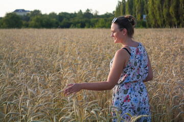 A woman in a wheat field looks at the harvest.