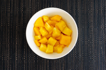 Exotic Fruit Delight: A white bowl filled with juicy pieces of pineapple and ripe mango arranged on a dark textured tablecloth