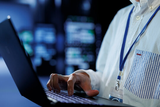 Tech support in data center uses laptop to prevent system overload during peak traffic periods. Hardworking expert in server farm ensuring enough network bandwidth for smooth operations, close up - Powered by Adobe