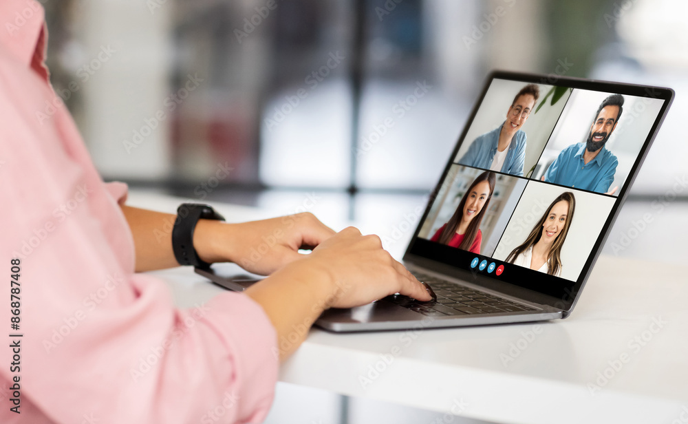 Poster a woman in a pink shirt sits at a desk and participates in a video conference meeting. she is using 