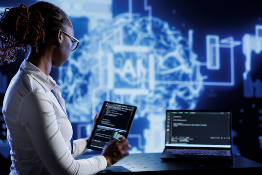 Computer scientist updates neural networks made of interconnected nodes, writing intricate binary code scripts on tablet and laptop. Server room expert uses programming to upgrade AI simulation model
