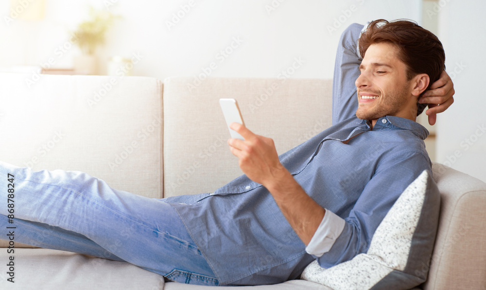 Poster A man is relaxing on a couch, using his smartphone. He is smiling and appears to be enjoying himself.