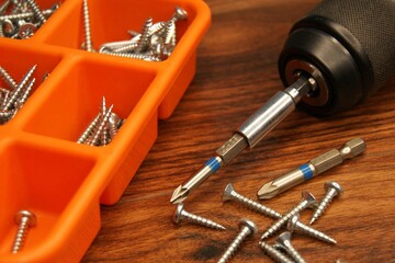 Red screw box and screw gun on a dark wooden table. Close-up of the craftsman's workplace.