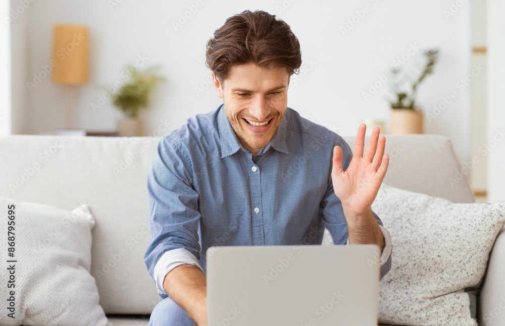 Poster a man sits on a couch, smiling and waving to the laptop screen in front of him.