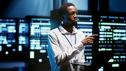 African american meticulous employee walking through server rows providing vast computing resources...