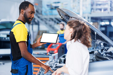 Mechanic in car service uses mockup tablet to order new engine for malfunctioning vehicle. Adept garage workspace expert shows woman needed parts replacement on isolated screen device