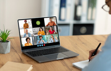 A person sits at a desk in a home office and attends a video conference meeting on their laptop...
