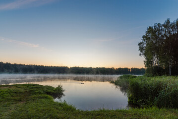 Fototapeta premium Small forest lake covered with fog at sunrise on June morning