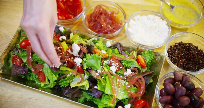 Adding feta cheese, olives and other ingredients to Romaine tomato salad