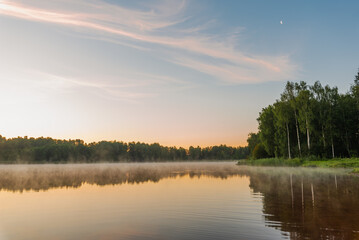 Small forest lake covered with fog at sunrise on June morning