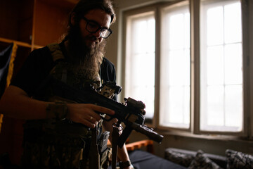 Portrait of bearded airsoft player with gun preparing for simulation.