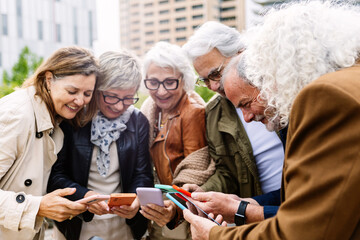 Senior group of people using mobile phone device standing in circle outdoors. Technology and baby boomers lifestyle concept - Powered by Adobe