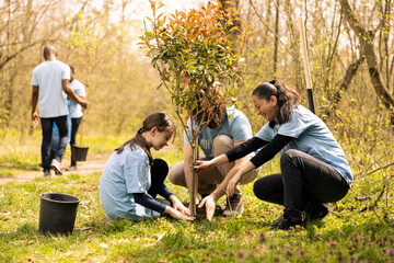 Volunteers and a little kid planting tree and covering hole in the ground, contributing to...