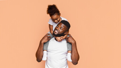 Happy African American father and his daughter posing together against a peach background. The...