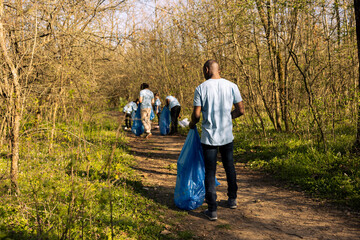 African american volunteer collecting garbage for community service, contributing to litter cleanup mission. Young adult preserving and clearing the natural forest environment. © DC Studio
